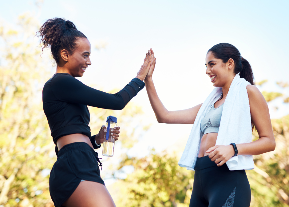 An image of 2 women outside, high-fiving each other after a summer workout, demonstrating the importance of having your guide to summer wellness.