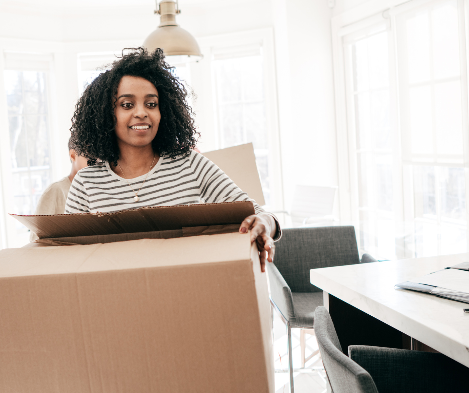 An image of a woman with a box in her arms at home, smiling,  demonstrating how fall decluttering boosts your health!