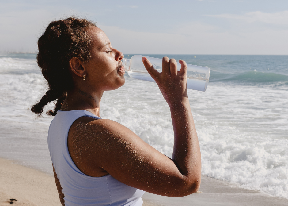 A woman on the back, drinking a bottle of water and looking healthy, demonstrating that she practices the 5 habits to optimize your health.