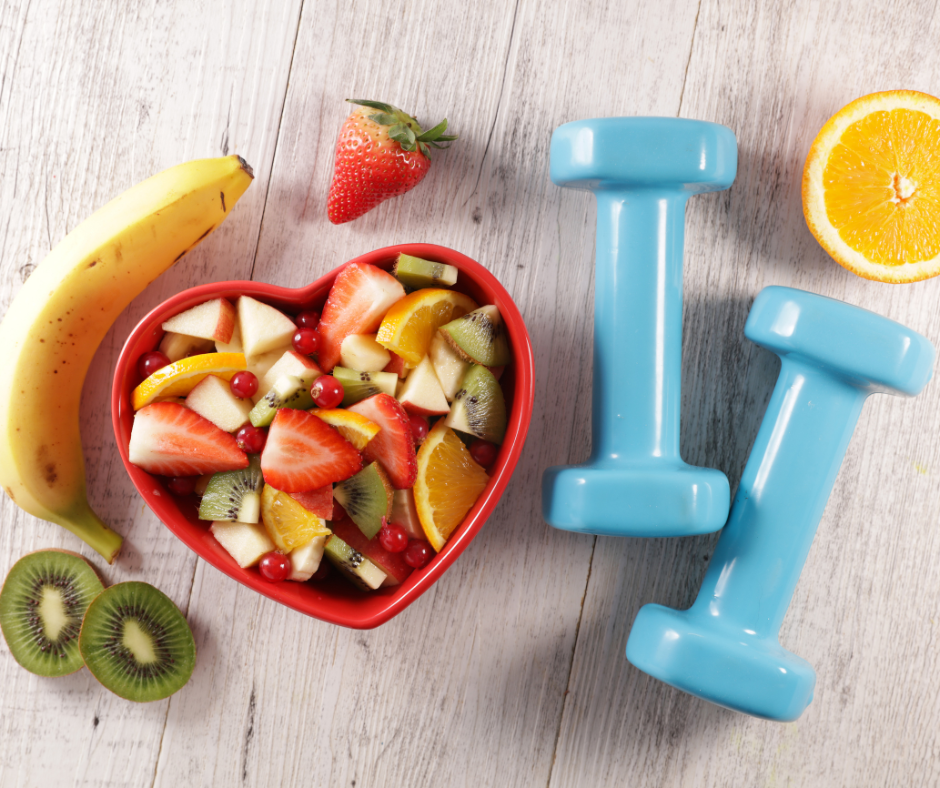 An image of fruit in a heart-shaped bowl and some small weights, demonstrating a few of the 5 habits to optimize your health.