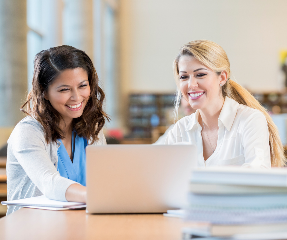An image of two woman, looking at their finances and smiling confidently, demonstrating how important financial wellness is for women to know and understand. 